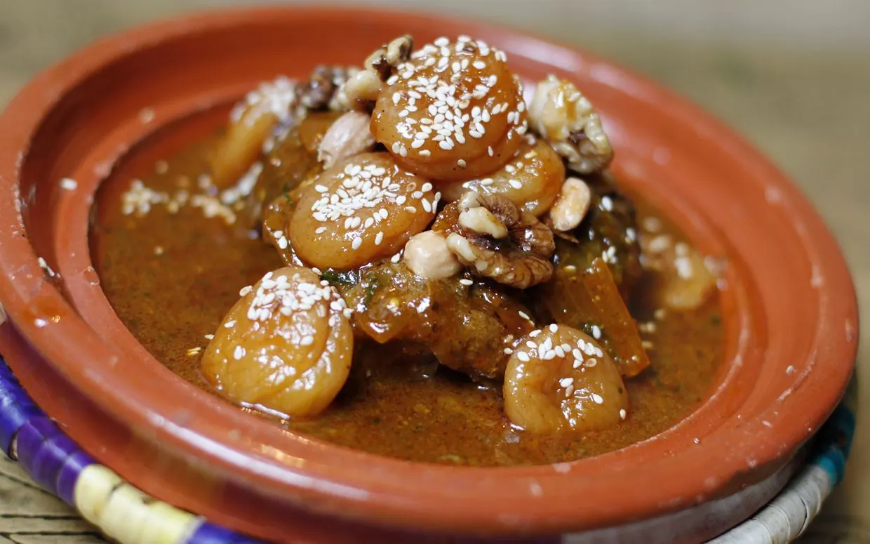 A clay tagine topped with caramelised fruit, walnuts and sesame